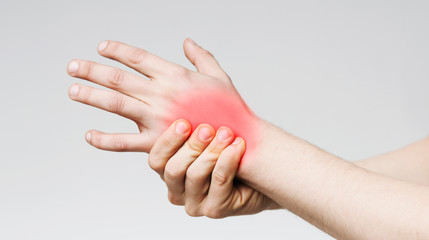 A person holding their left wrist with their right hand, with a red area highlighted on the wrist, indicating pain or inflammation from repetitive stress injuries, against a plain light background.