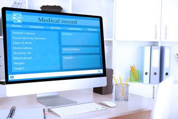 A computer monitor displays a digital medical record form to document injuries claim details, with fields for patient information in an office setting with folders, pencils, and cabinets in the background.