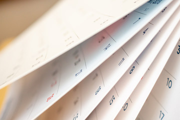 Close-up of calendar pages being flipped, illustrating the passage of time—a subtle nod to delay settlement in personal injury cases—with dates and numbers in blue and red under bright, soft-focused lighting.