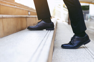 A person, after falling down broken stairs, is seen wearing black dress shoes and black pants while walking up outdoor stone steps, with only their lower legs and feet visible.