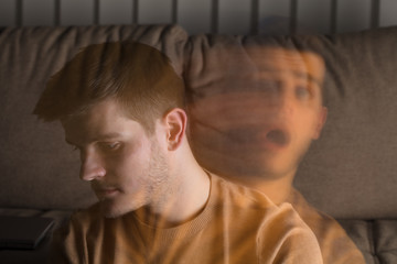 A man sits on a couch looking down pensively, while a faded, ghost-like image of himself appears beside him, showing distress—reflecting inner turmoil and anxiety often experienced after a car accident or living with PTSD.