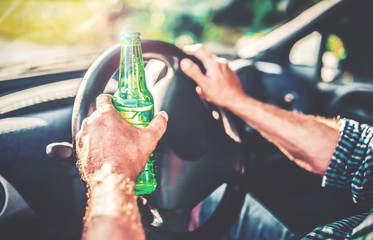 A person driving a car is holding a green glass bottle in one hand and gripping the steering wheel with the other, suggesting the dangerous act of drinking alcohol while driving—and highlighting why victims seek compensation if hit by a drunk driver.